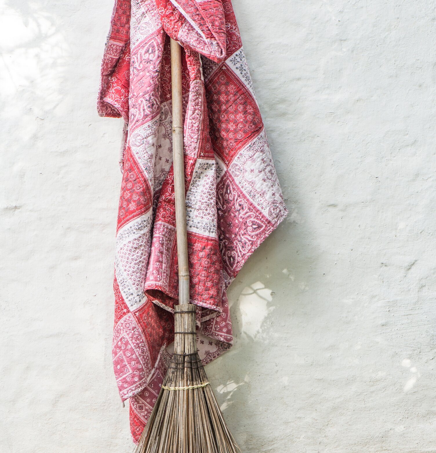 Foto av charmig röd pläd i patchwork-stil mot vit vägg