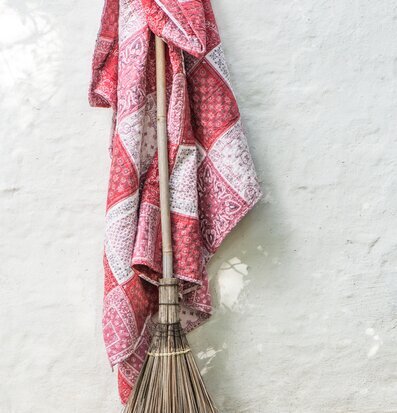 Foto av charmig röd pläd i patchwork-stil mot vit vägg