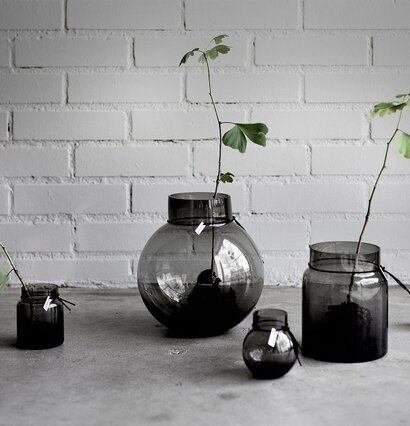 Glasvas Rund Rökgrå från Ernst på betongyta med tegelvägg