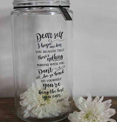 Bild av stilren glaslykta med text och vita blommor