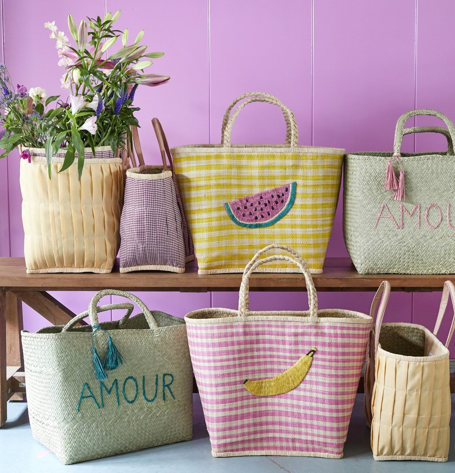 Väska Check Raffia L från Rice på träbänk med lila vägg