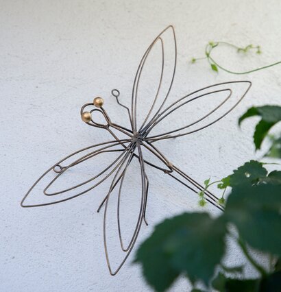 Foto av smideskonst: Trollslända på vägg med grönska