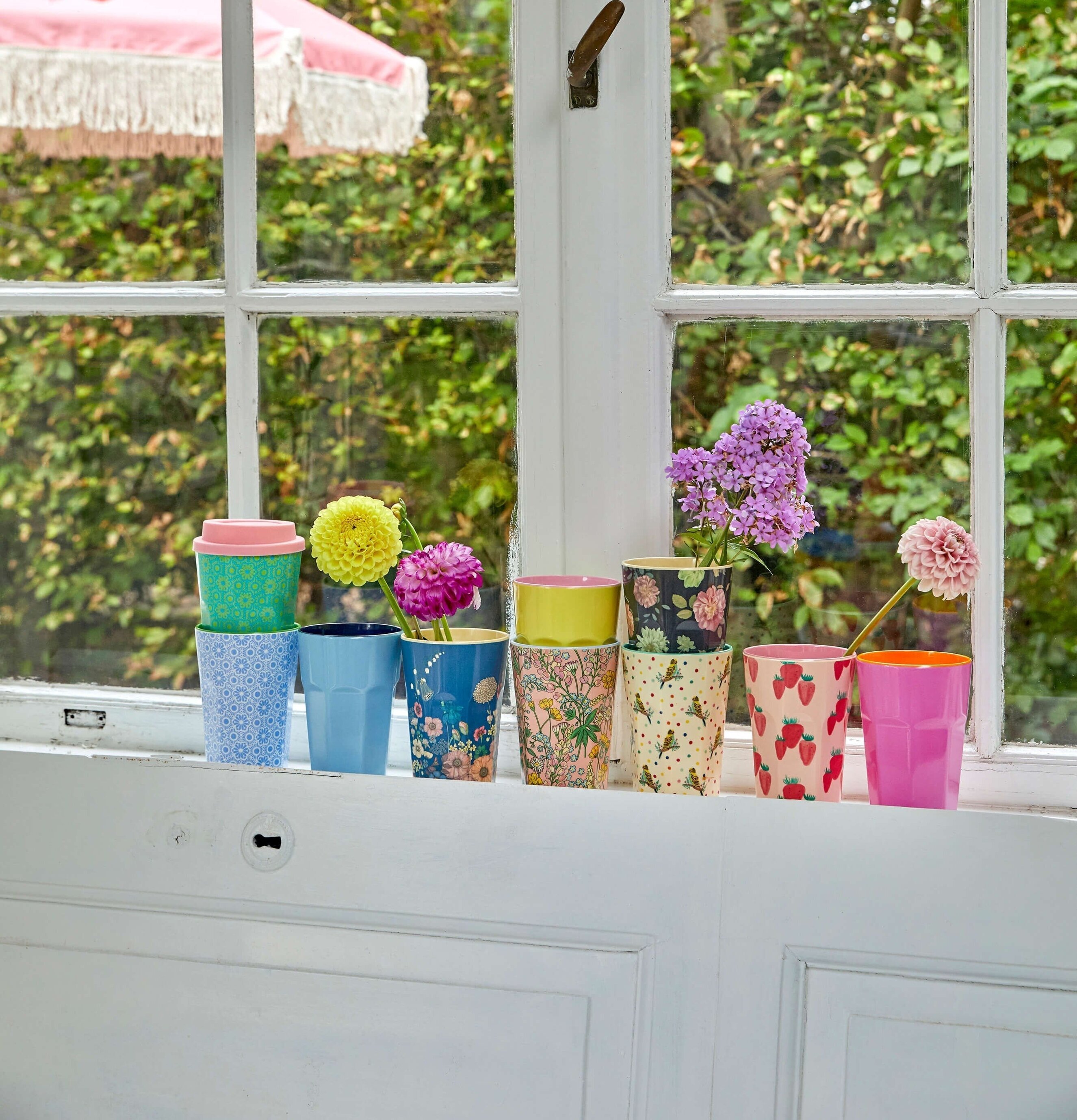 Bild av färgglada muggar på fönsterbräda med blommor