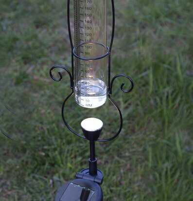 Bild av solcellsdriven regnmätare i trädgårdsmiljö