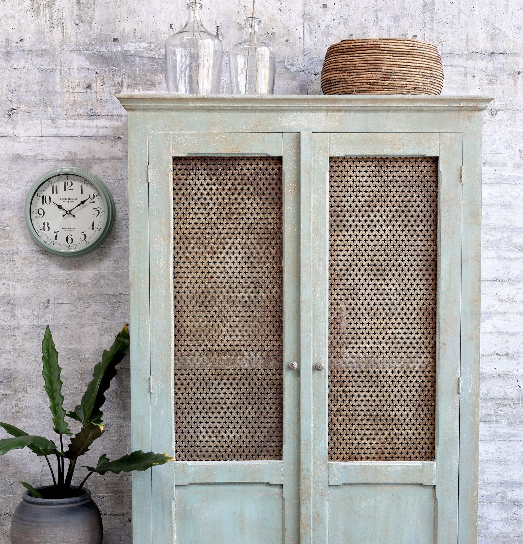 Väggklocka Verte från Chic Antique mot betongvägg med växt