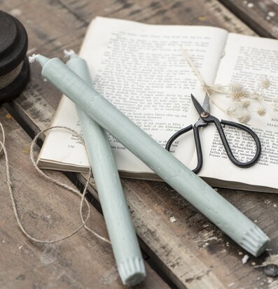 Bild av gröna ljus på rustikt bord med bok och saxar