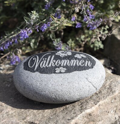 Foto av natursten med Välkommen i trädgårdsmiljö