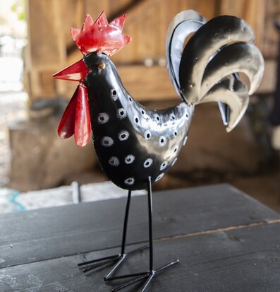 Bild av svart tupp i hamrad plåt med röda detaljer