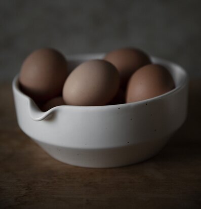 Bild av stilren skål i naturvitt med ägg i fokus