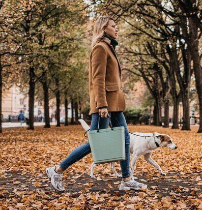Bild av kvinna med hund i höstpark med stilren väska