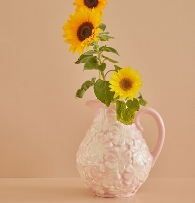 Bild av rosa kanna med blommor och solrosor