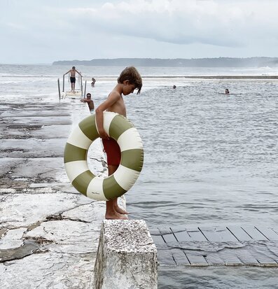 Bild av barn vid havet med badring och molnig himmel