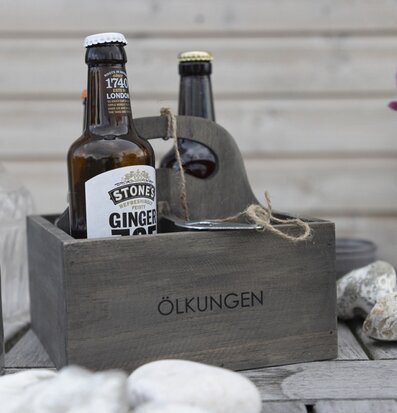 Bild av grå trälåda med drycker och dekorativa inslag