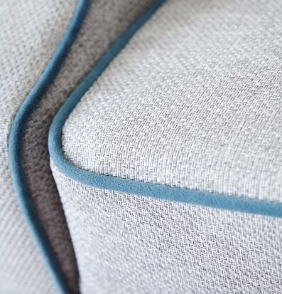 Bild av fåtölj med grått tyg och petrolblå kantband