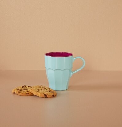 Bild av en mintfärgad mugg med kakor på beige yta