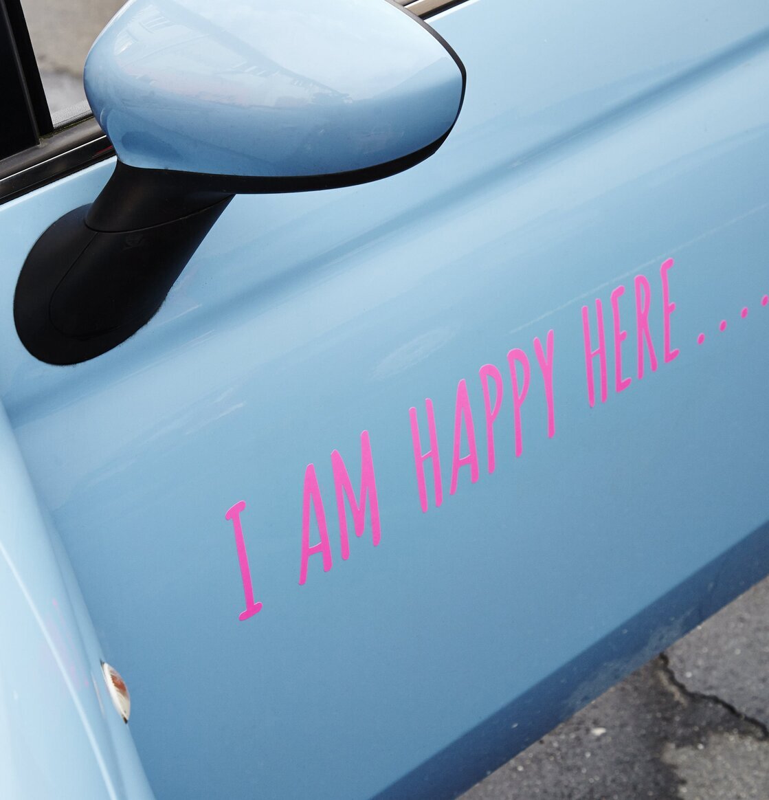 Bild av ljusblå bildörr med rosa text I AM HAPPY HERE
