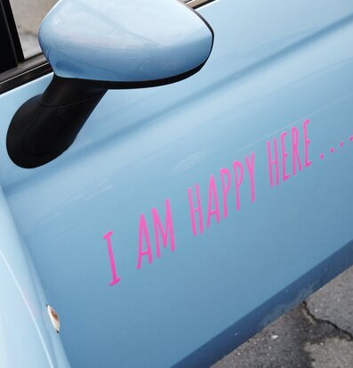 Bild av ljusblå bildörr med rosa text I AM HAPPY HERE