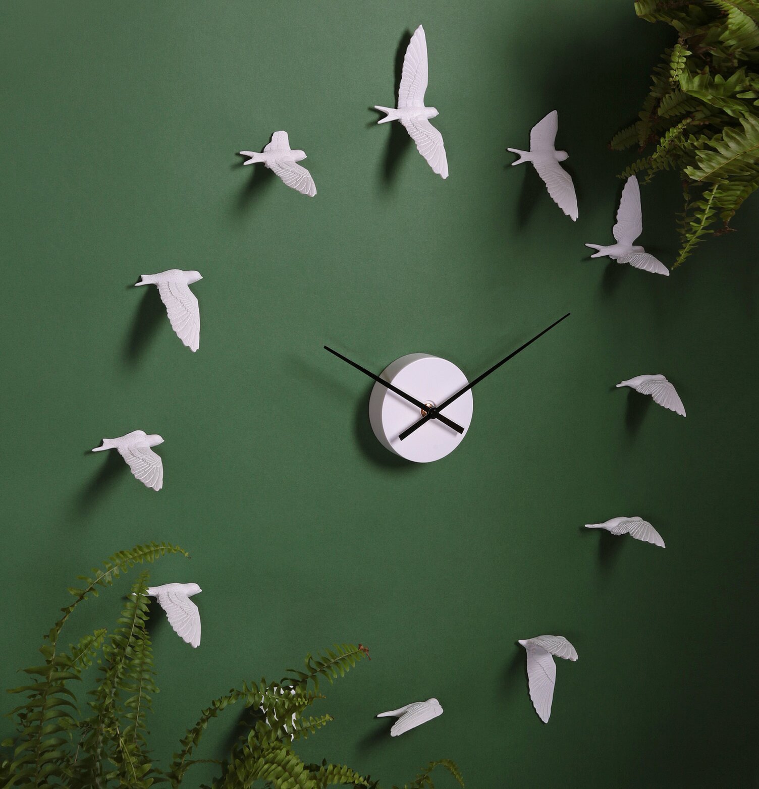 Väggklocka Swallow - Haoshi Design på grön vägg med växter