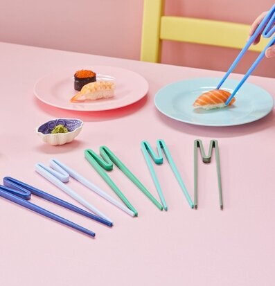 Bild av färgglada ätpinnar på rosa bord med sushi