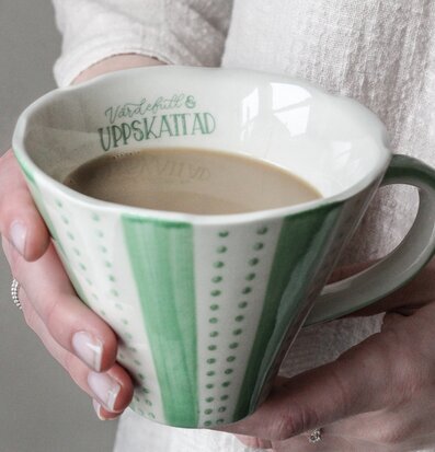 Bild av mugg med grön-vit design och textdetaljer
