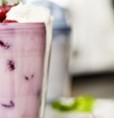 Bild av rosa milkshake med grädde och bär i fokus