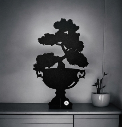 Bild av stilrent bonsaiträd i svart plåt och krukväxt