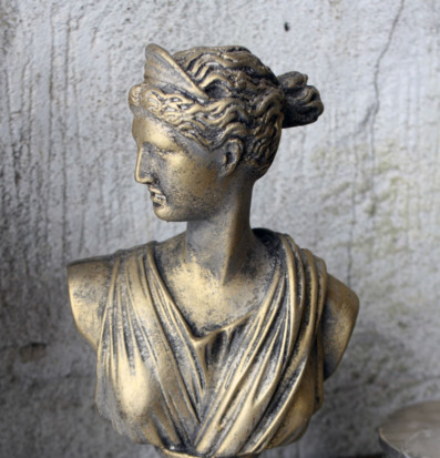 Bild av dekorativ antikguldfärgad byst mot betongvägg