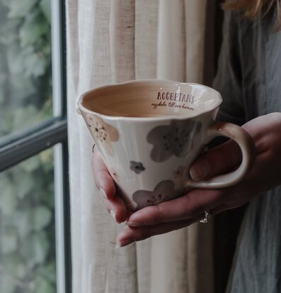 Bild av keramikmugg med blommotiv och inspirerande text