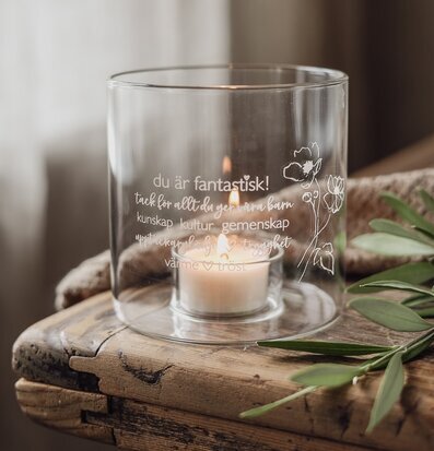 Bild av ljuslykta i glas med ingraverad text och blomster