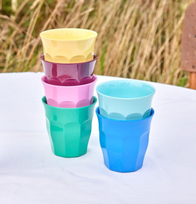 Bild med färgglada staplade muggar utomhus på vit duk