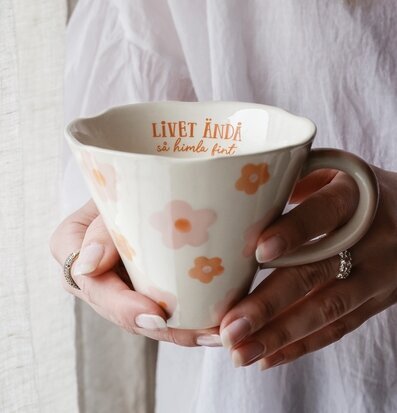 Bild på hand med blomstrande mugg i mjuka pastellfärger