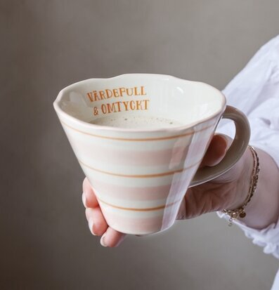 Bild på hand som håller randig pastellmugg med varm dryck