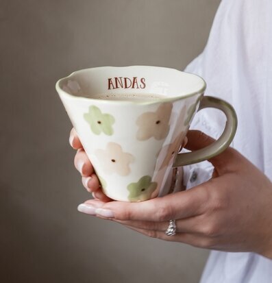Bild på hand som håller mugg med texten ANDAS och blommönster