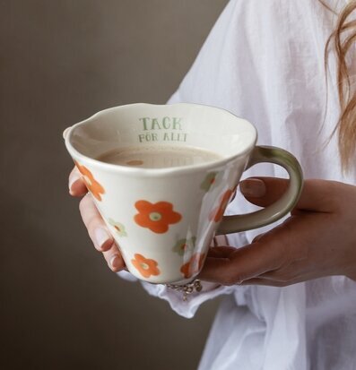 Bild på hand som håller mugg med blommor och grön text