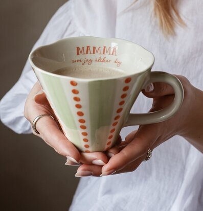 Bild på hand som håller mugg med kärleksfull text och mönster