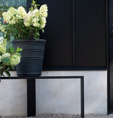 Bild av svart kruka på stativ i stilren utomhusmiljö