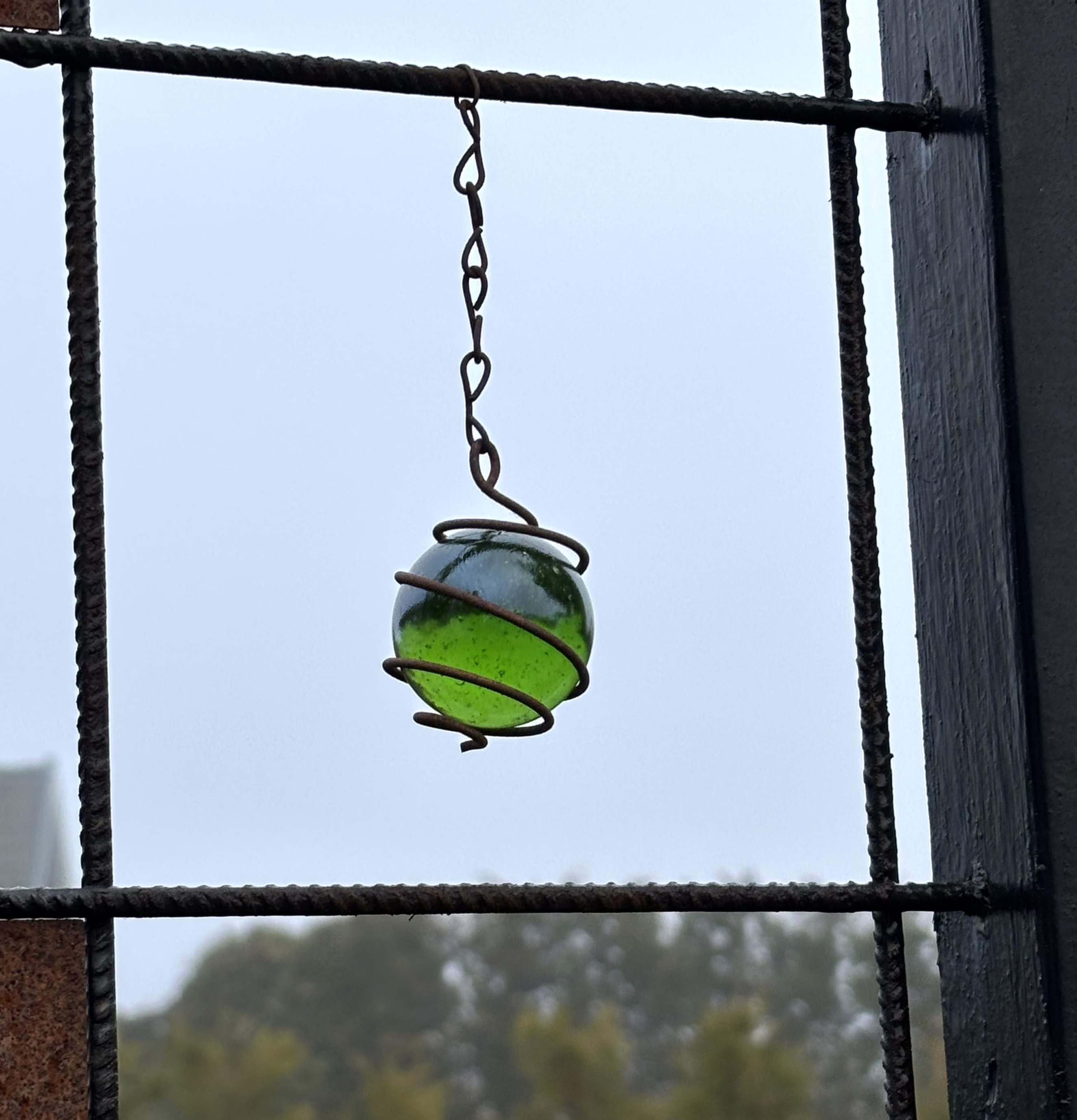 Bild av hängande grön glaskula i armeringsnät utomhus