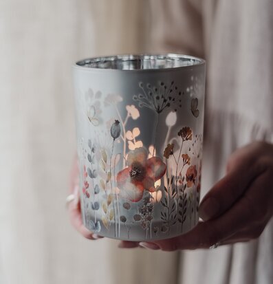 Bild av hand som håller lykta med ängsblommor och värmeljus