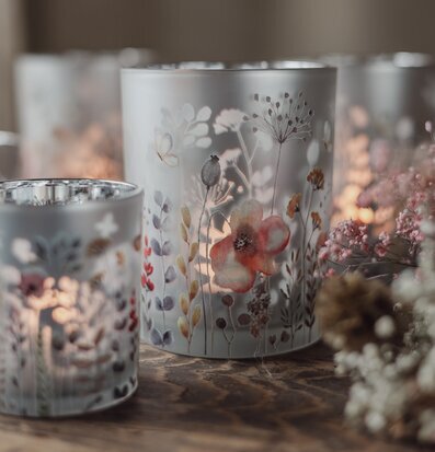 Bild av ljuslyktor med blommotiv på träbord i somrig miljö