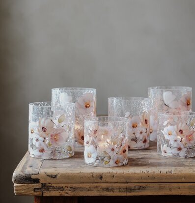 Bild med sju glaslyktor och blommor på rustikt träbord