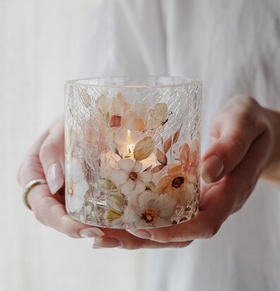 Bild av ljuslykta med blommor och sprucket glas i mjuka toner