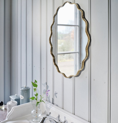 Bild på ljust badrum med vågig spegel och klassiskt handfat