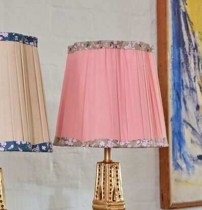 Bild på rosa lampskärm med blommig kant och guldfärgad fot