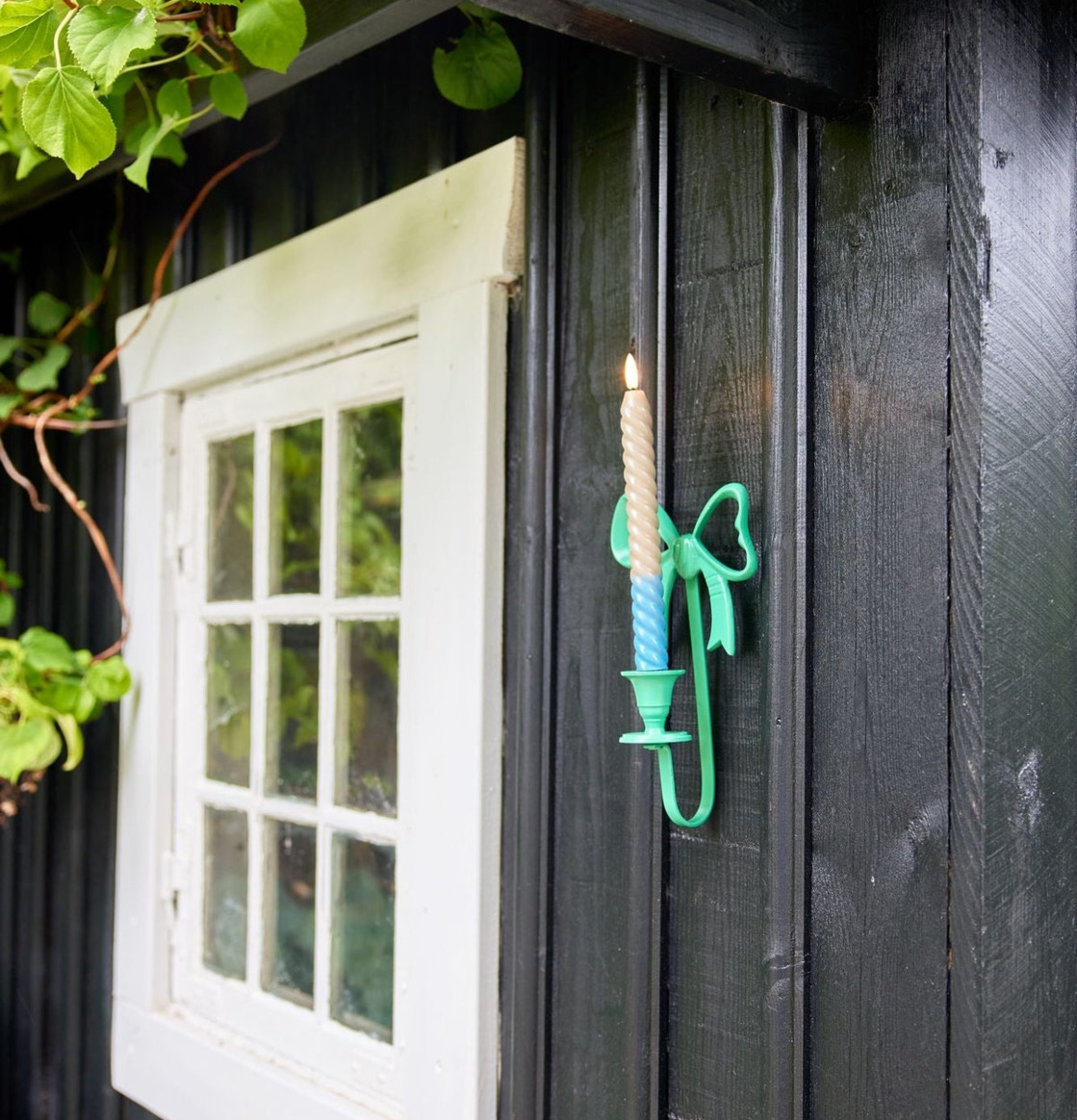 Bild av svart träfasad med grön ljusstake och gröna växter