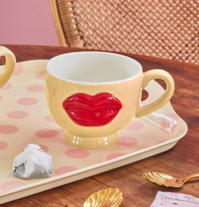 Bild av gul keramikkopp med röda läppar och rosa fat