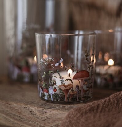 Bild av glaslykta med svampmotiv och mjukt ljus på träbord