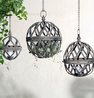 Bild på tre hängande klotlyktor i metall med växtdetaljer