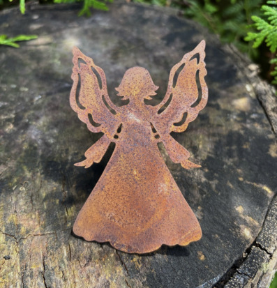 Bild av rostig ängel i metall på stubbe med grönskande bakgrund