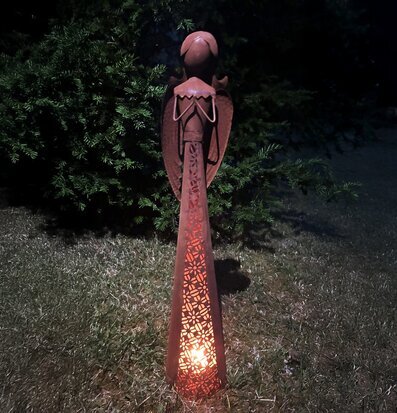 Bild av rostig ängelskulptur med ljuslykta i kvällsträdgård