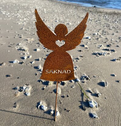 Bild av rostig ängeldekoration med hjärta och text på strand